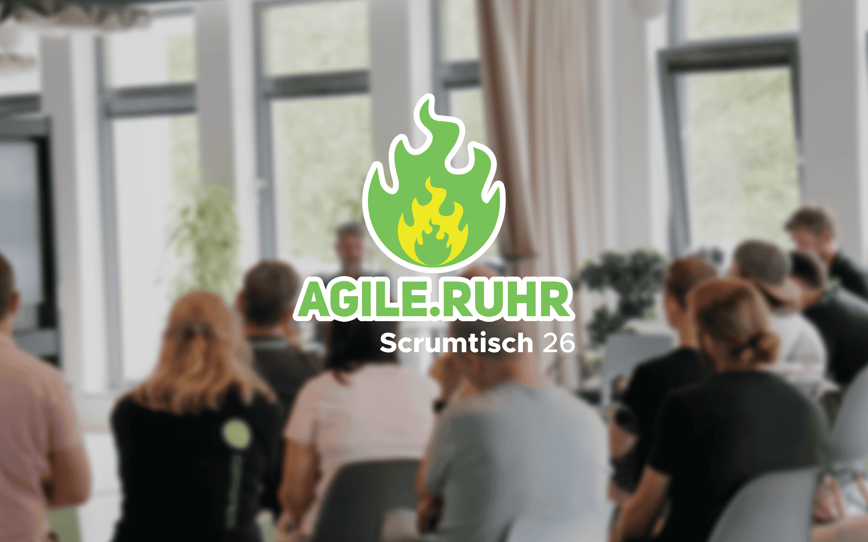 A blurry photo of an event showing participants seated in a brightly lit room. In the center is the “AGILE.RUHR” logo featuring a green flame, along with the text “Scrumtisch 26.”
