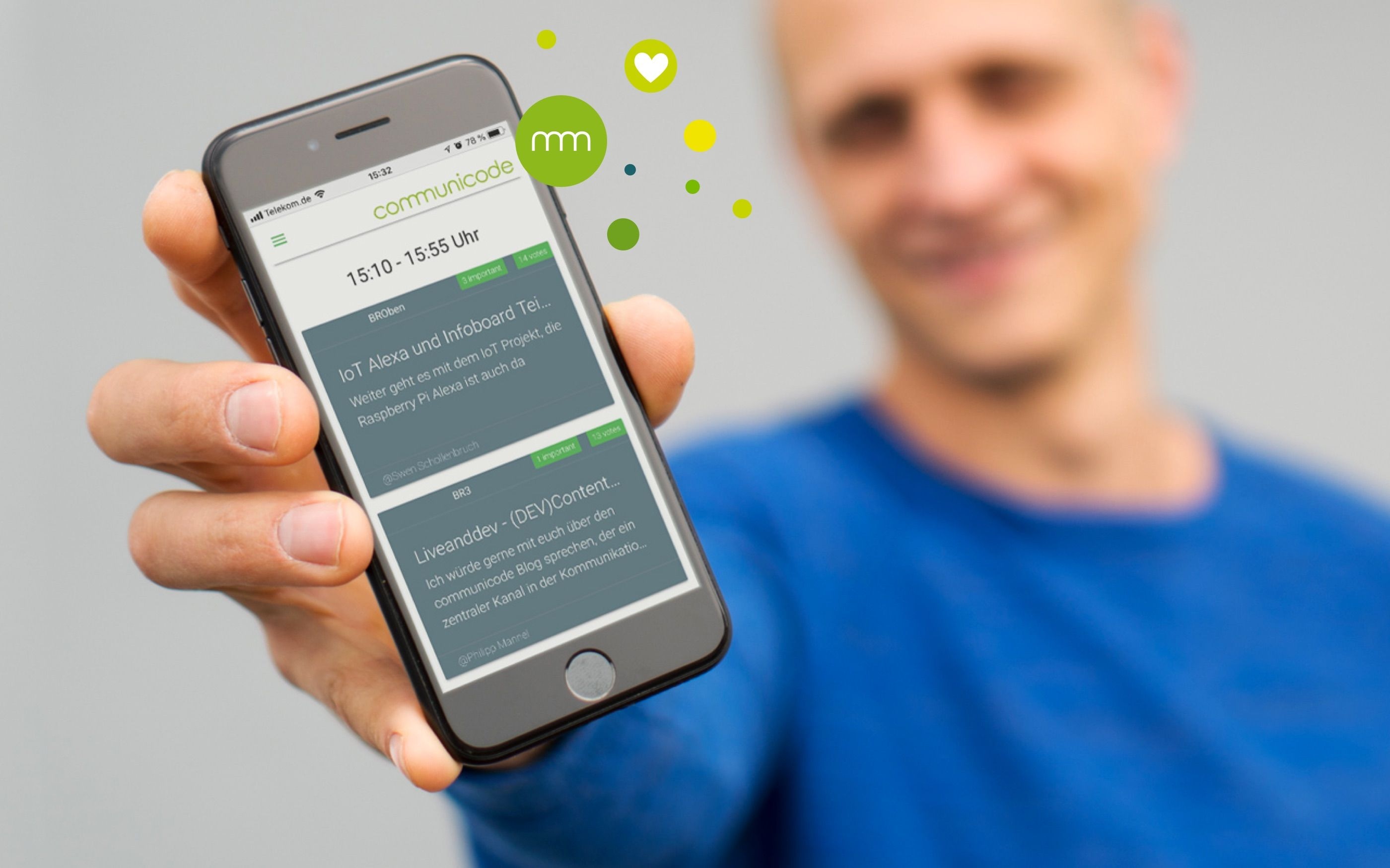 Ein Mann, verschwommen im Hintergrund hält ein klar zu sehendes Handy in die Kamera, auf dem eine App zu erkennen ist.