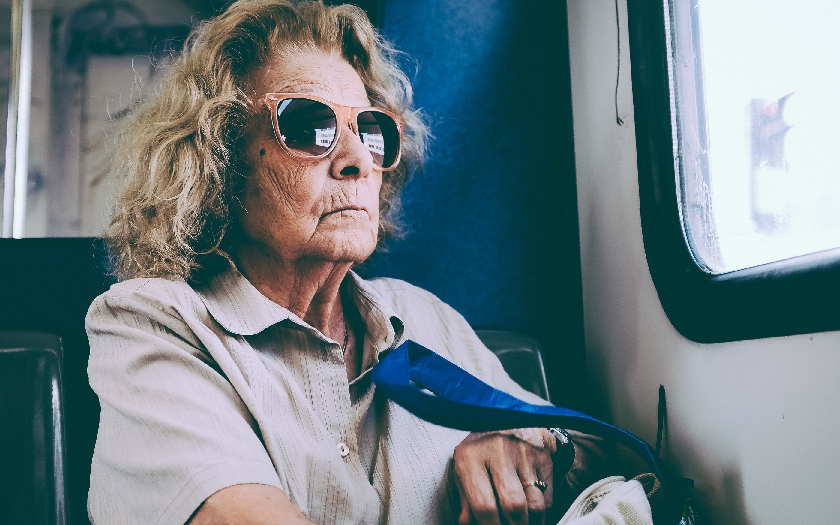Photo of an elderly lady wearing sunglasses on a train, looking somewhat grim.