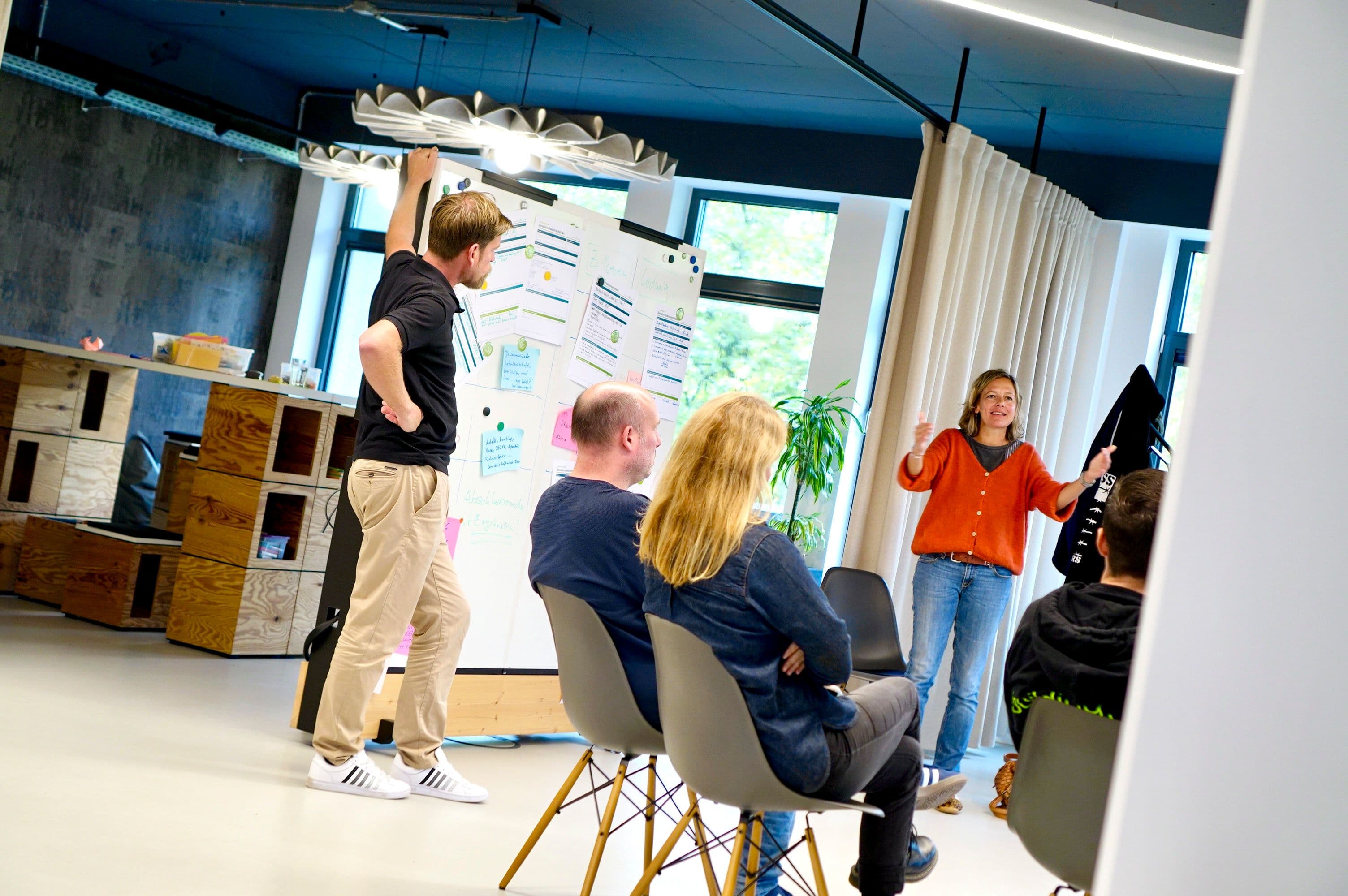 Workshop-Teilnehmende diskutieren vor einem Whiteboard mit Notizen und Arbeitsergebnissen in einem modernen Seminarraum.
