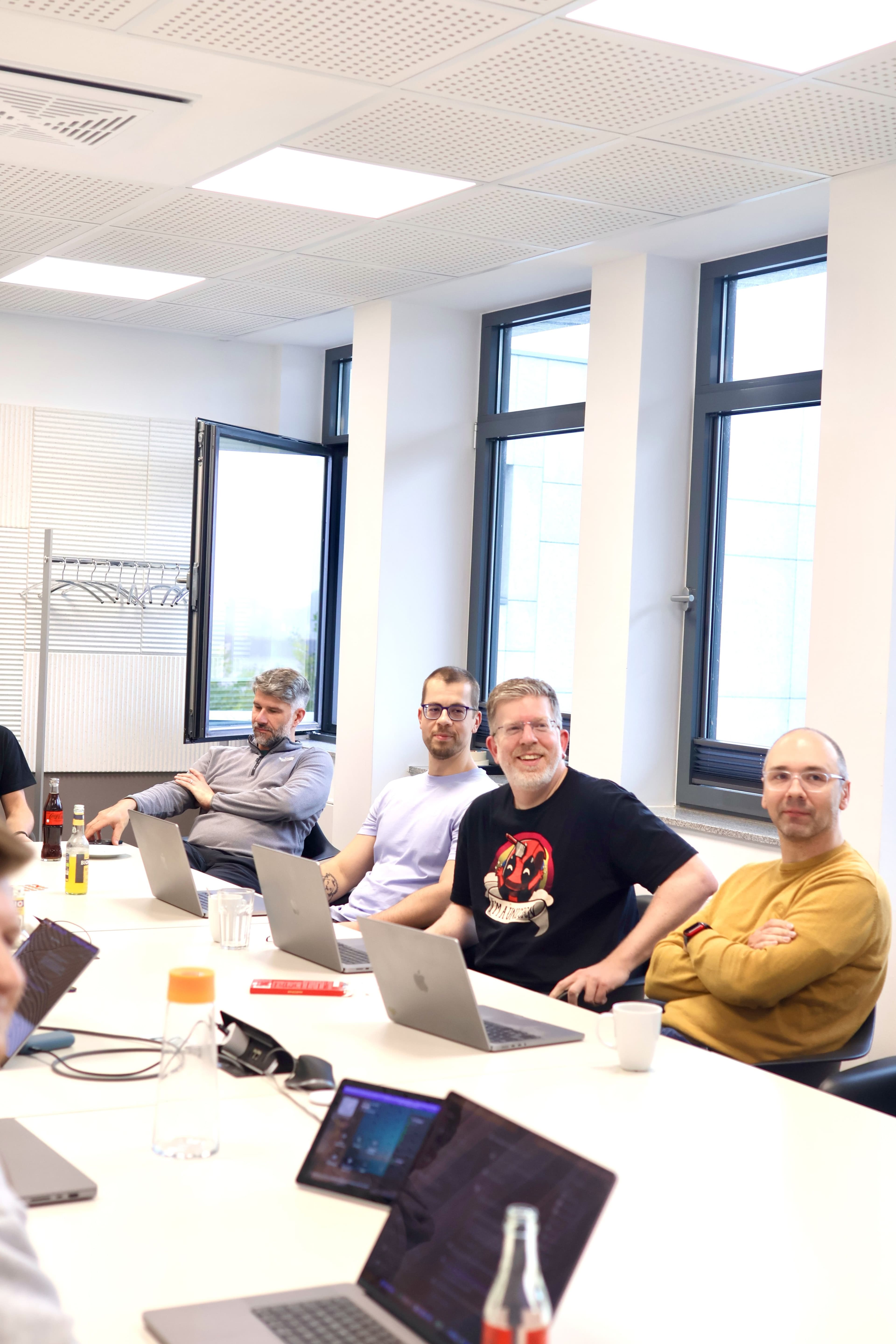 Workshop participants sit with laptops around a conference table in a bright meeting room.