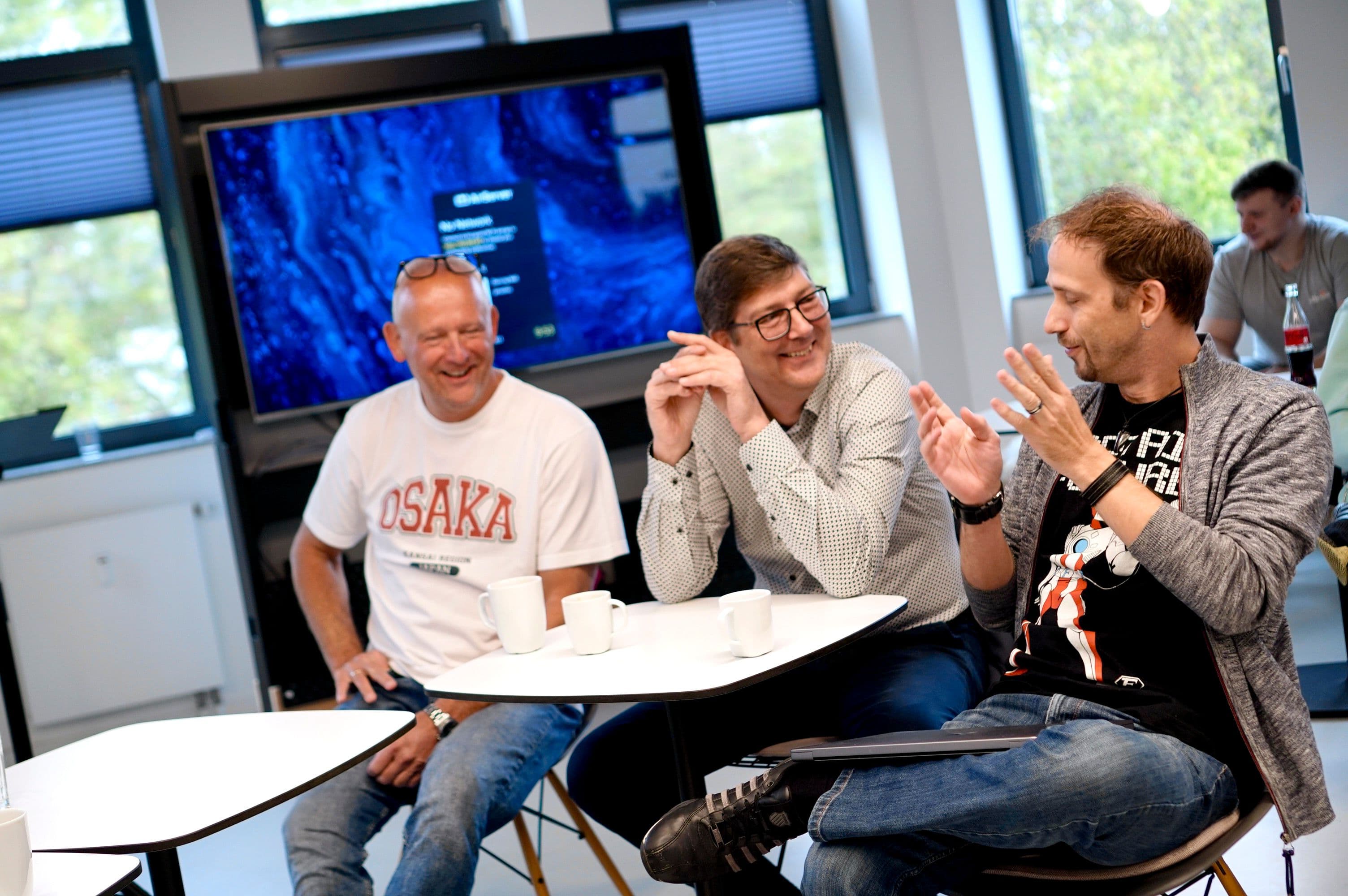 Workshop participants sit at small tables and exchange ideas during a discussion session in front of a large display screen.