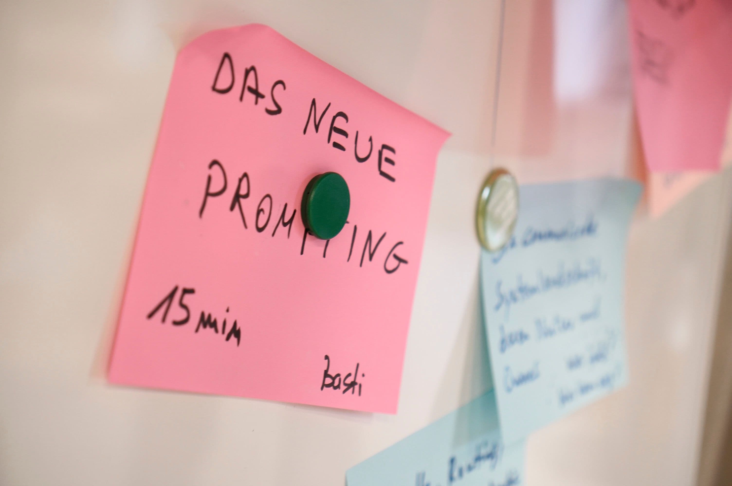 Haftnotiz mit dem Text „Das neue Prompting“ an einem Whiteboard befestigt, umgeben von weiteren Notizen für die Workshop- oder Projektplanung.
