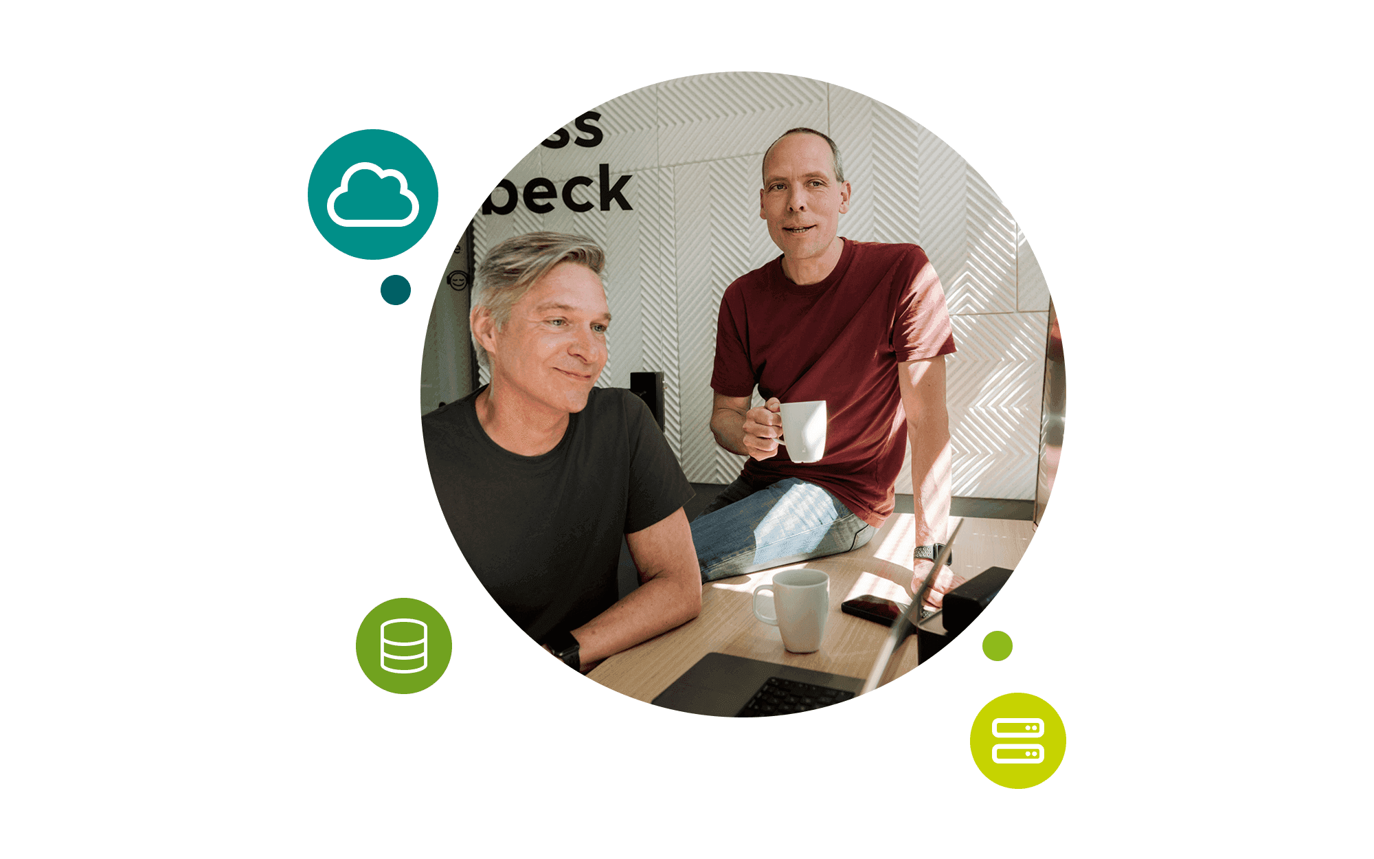 Two men at a desk, one sitting in front of it, one sitting on it holding a coffee cup.