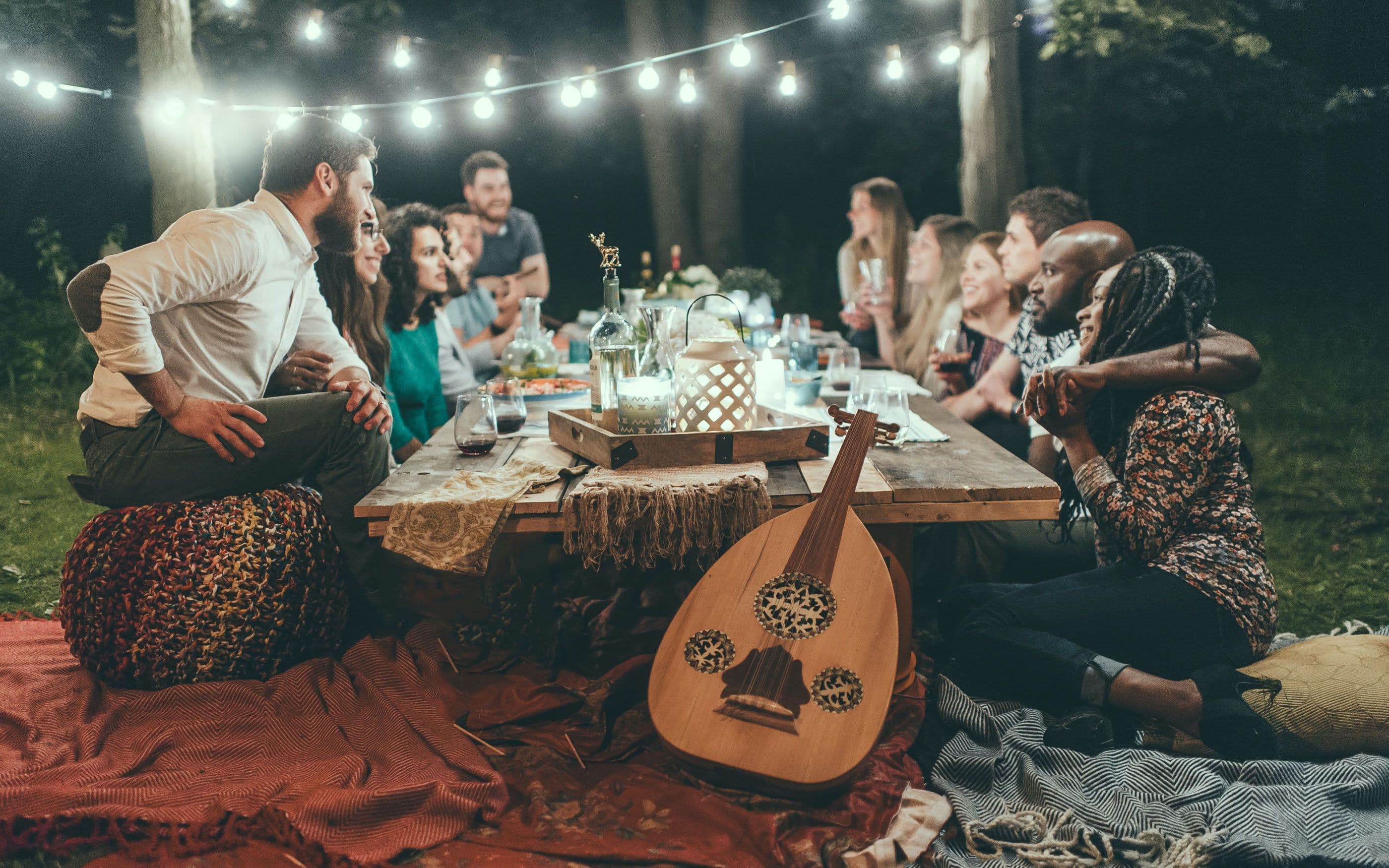 Foto Tisch mit vielen Menschen und Musikinstrument im Wald unter Lampions